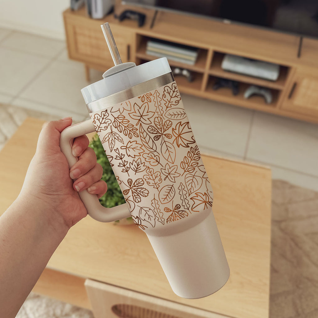 40 oz tumbler held by hand, cream base with orange leaf pattern and straw lid