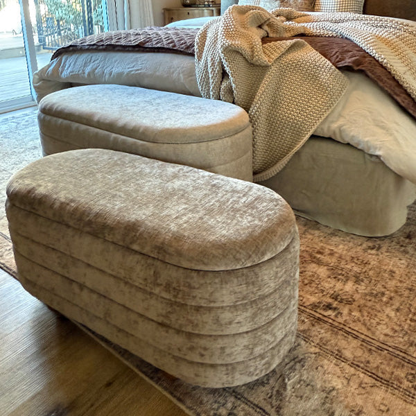 Upholstered storage bench with rounded cushioned lid and light beige fabric with stitched seams