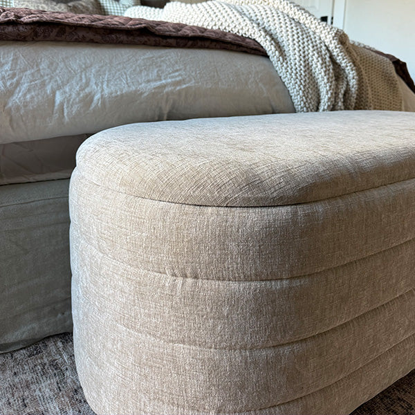 Close-up of light beige upholstered storage bench with rounded stitched cushion top
