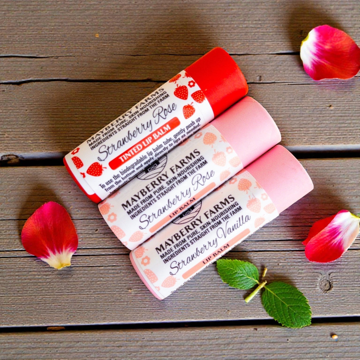 Mayberry Farms Strawberry Rose lip balm tubes with pink and red caps, with petals
