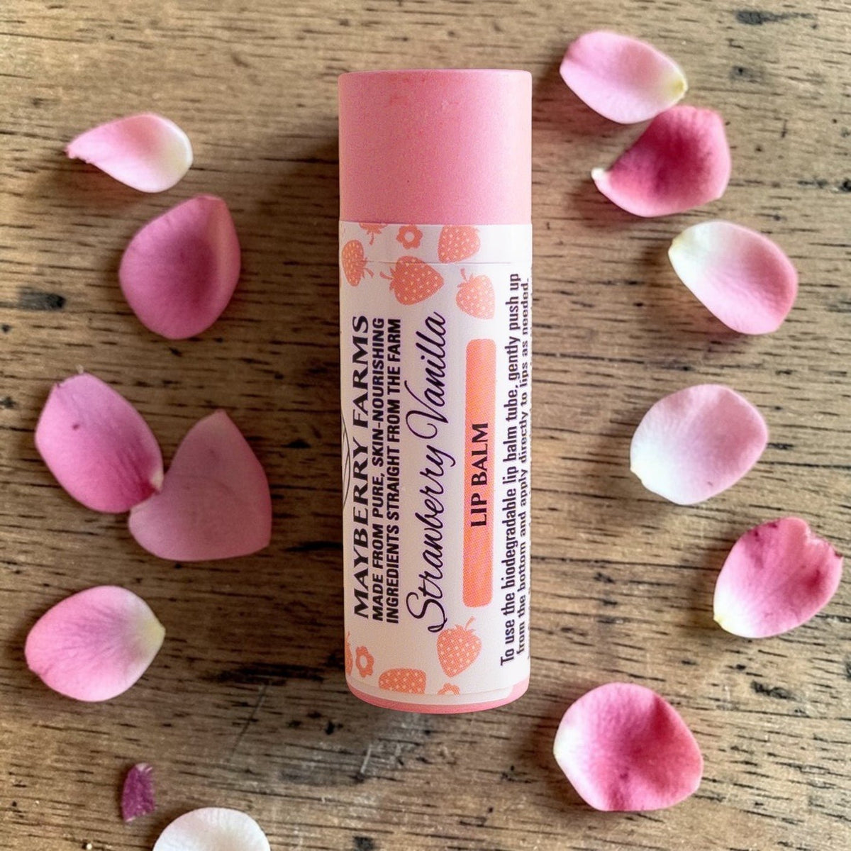 Mayberry Farms Strawberry Vanilla lip balm tube with pink body, surrounded by petals