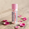 Strawberry Rose lip balm tube with pink body and cap, with scattered petal accents