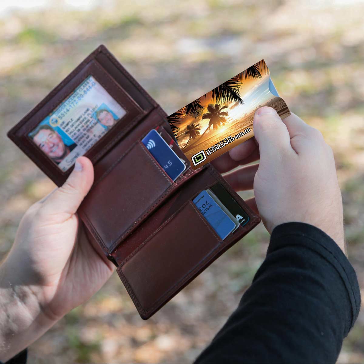 Brown multi-card wallet holding credit cards and an RFID shield sleeve outdoors