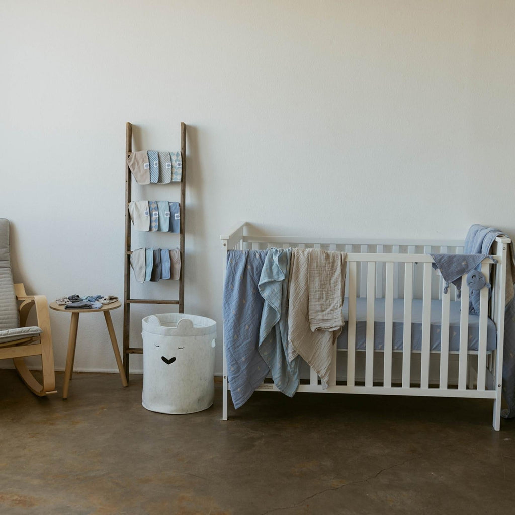 Crib with draped light blue and beige muslin swaddle blankets and folded extras