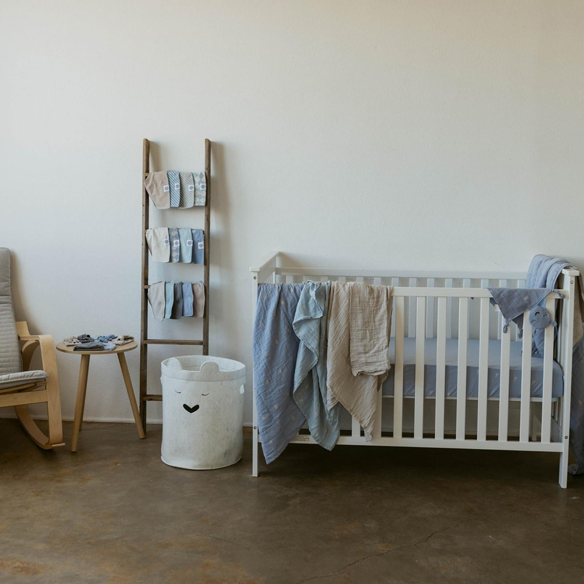 Crib with draped light blue and beige muslin swaddle blankets and folded extras