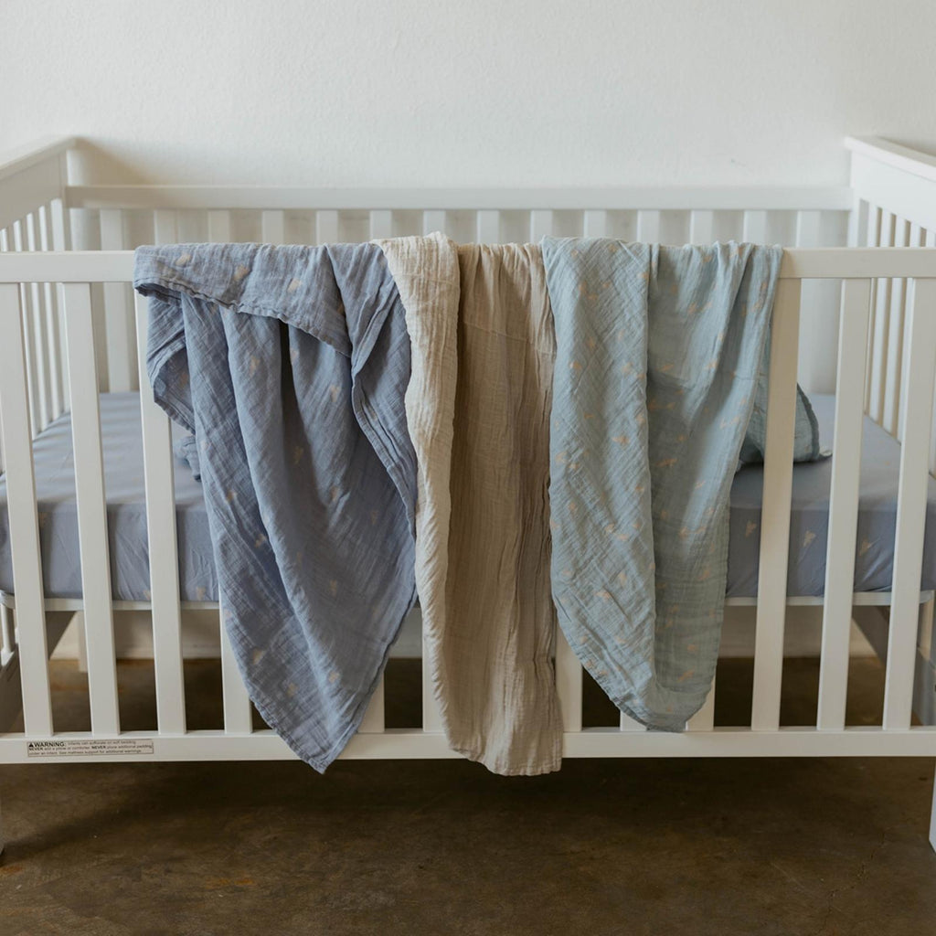Crib display of three muslin swaddle blankets in light blue and beige, cloud prints