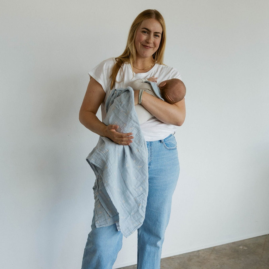 Light blue muslin swaddle blanket with cloud and bird print, baby wrapped on shoulder