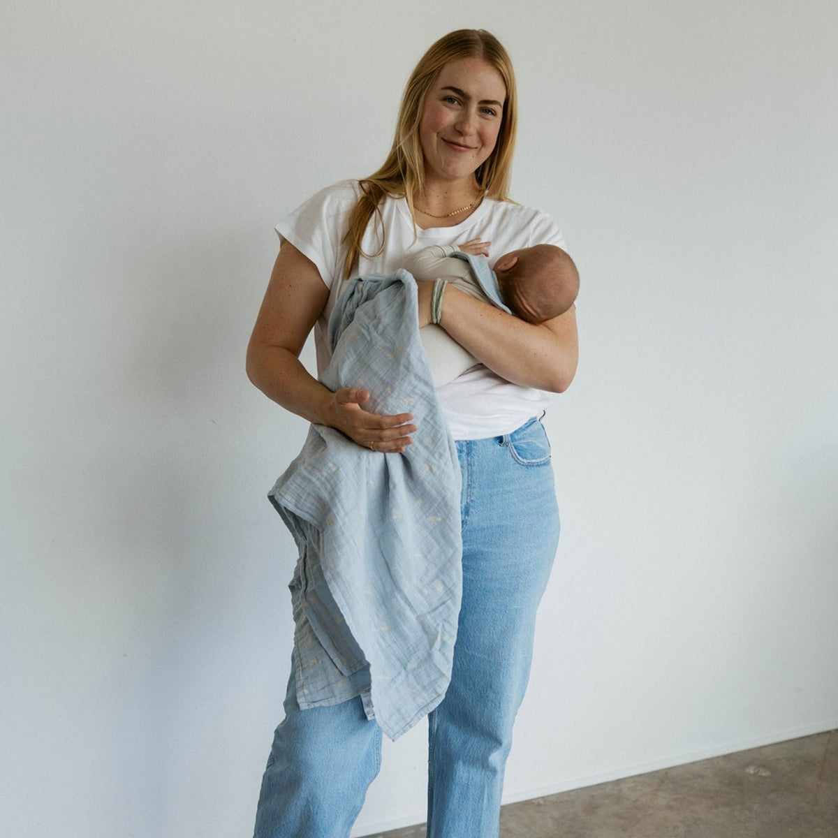 Light blue muslin swaddle blanket with cloud and bird print, baby wrapped on shoulder