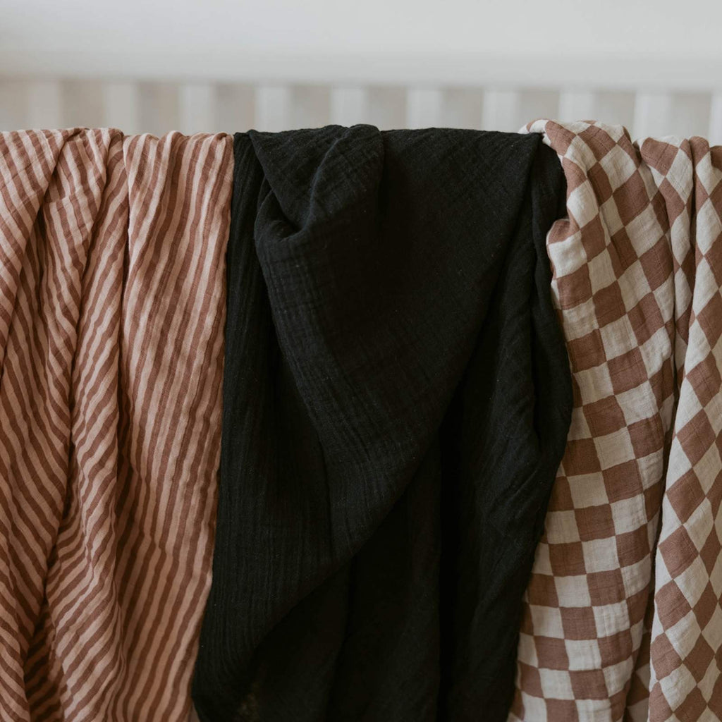 Three folded swaddles: rose-and-cream stripes, dark solid, and brown checkered fabric