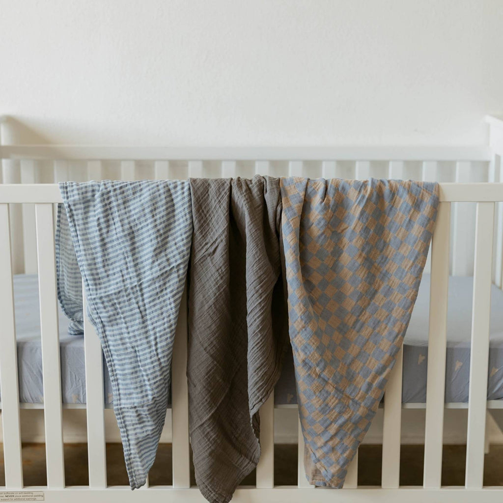 Stormy swaddle set swaddles draped over crib rail: blue check, gray, and blue striped