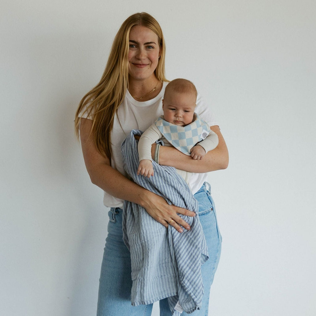 Baby wrapped in a blue and light plaid swaddle blanket, held by adult