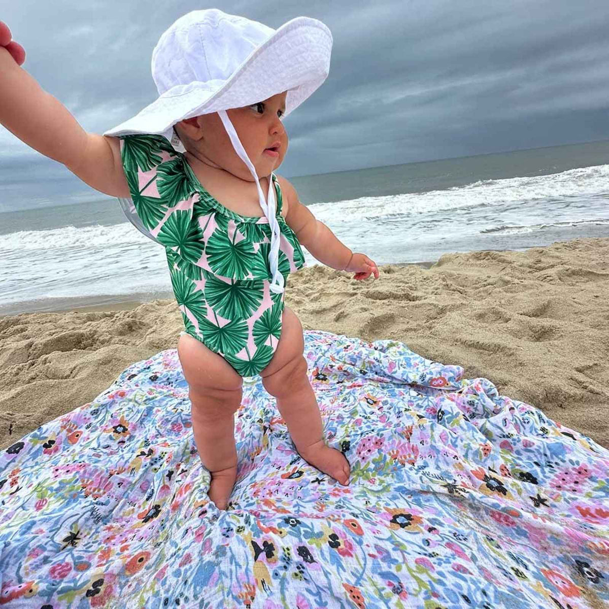 Floral baby blanket draped over a child outdoors on sand