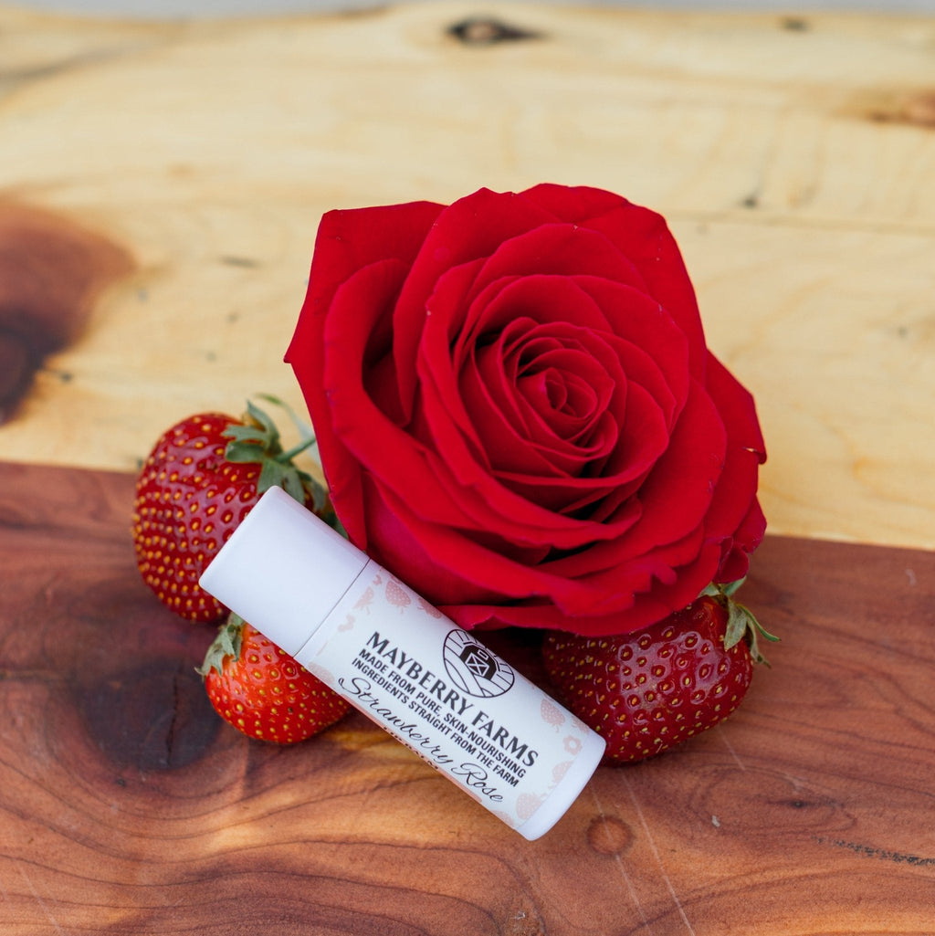 Mayberry Farms Strawberry Rose lip balm tube with red cap, beside a red rose