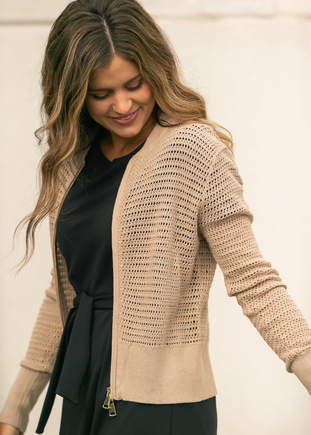 Beige open-knit crochet cardigan with long sleeves and zip-front closure over a top