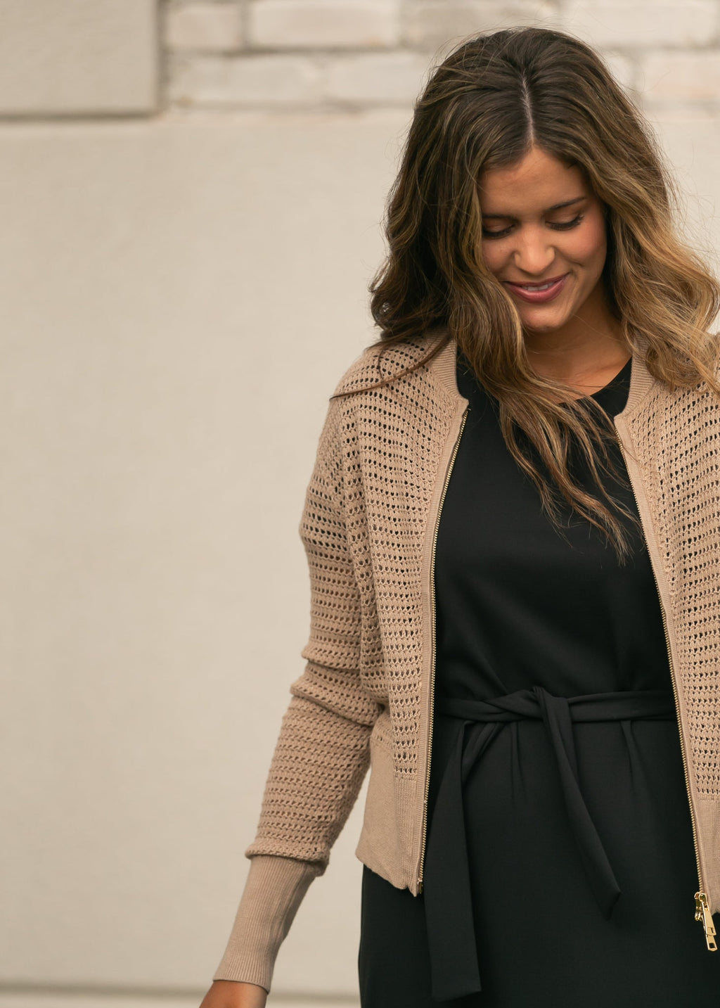Open-knit beige cardigan with zipper front and long sleeves, worn over dark top and dress.