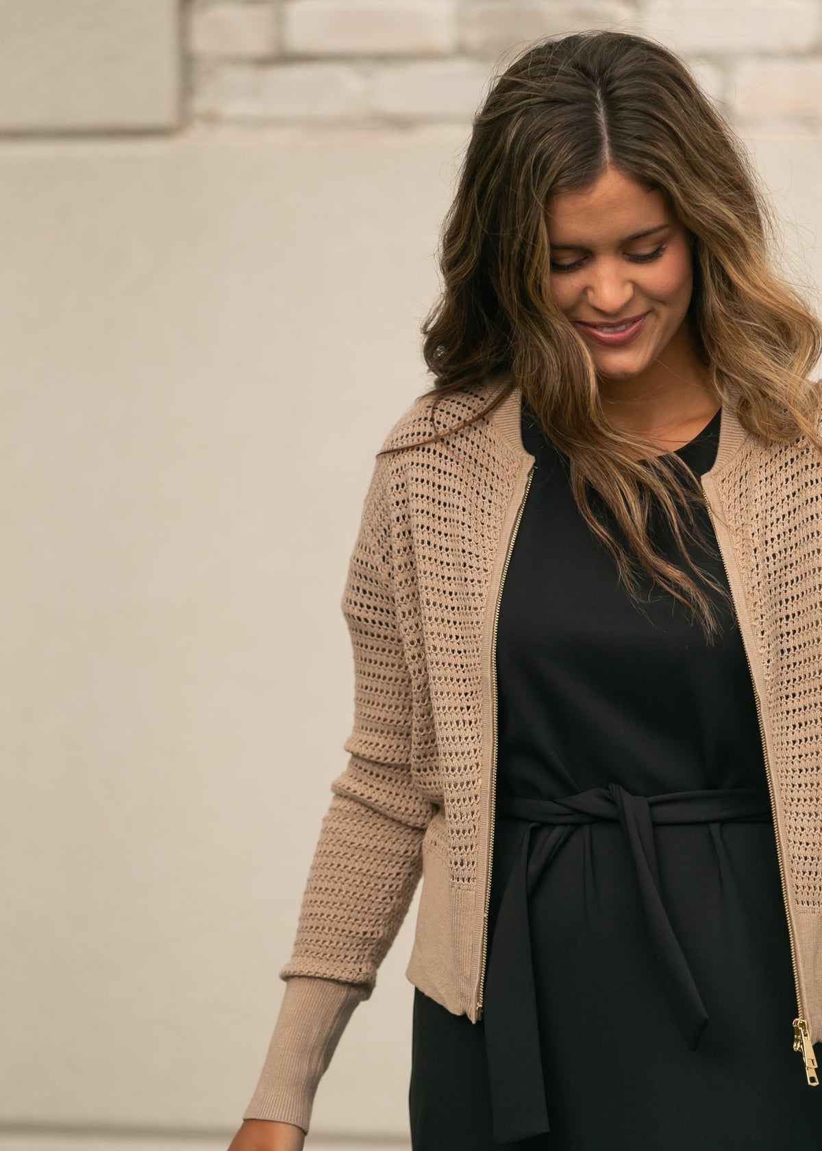 Open-knit beige cardigan with zipper front and long sleeves, worn over dark top and dress.