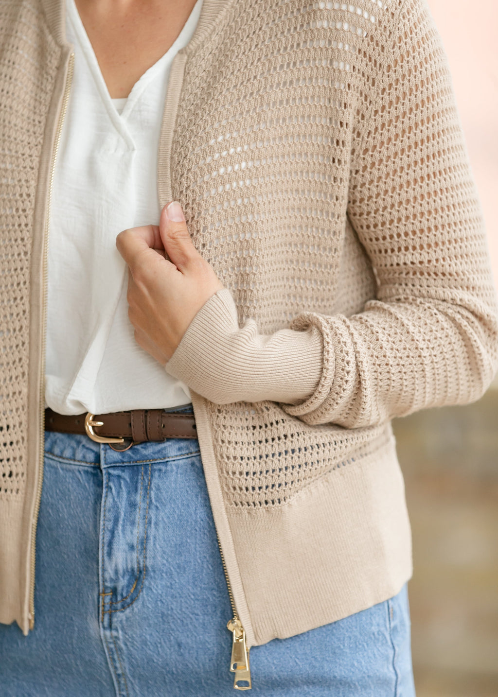 Close-up of beige open-knit cardigan with gold zipper and long sleeves
