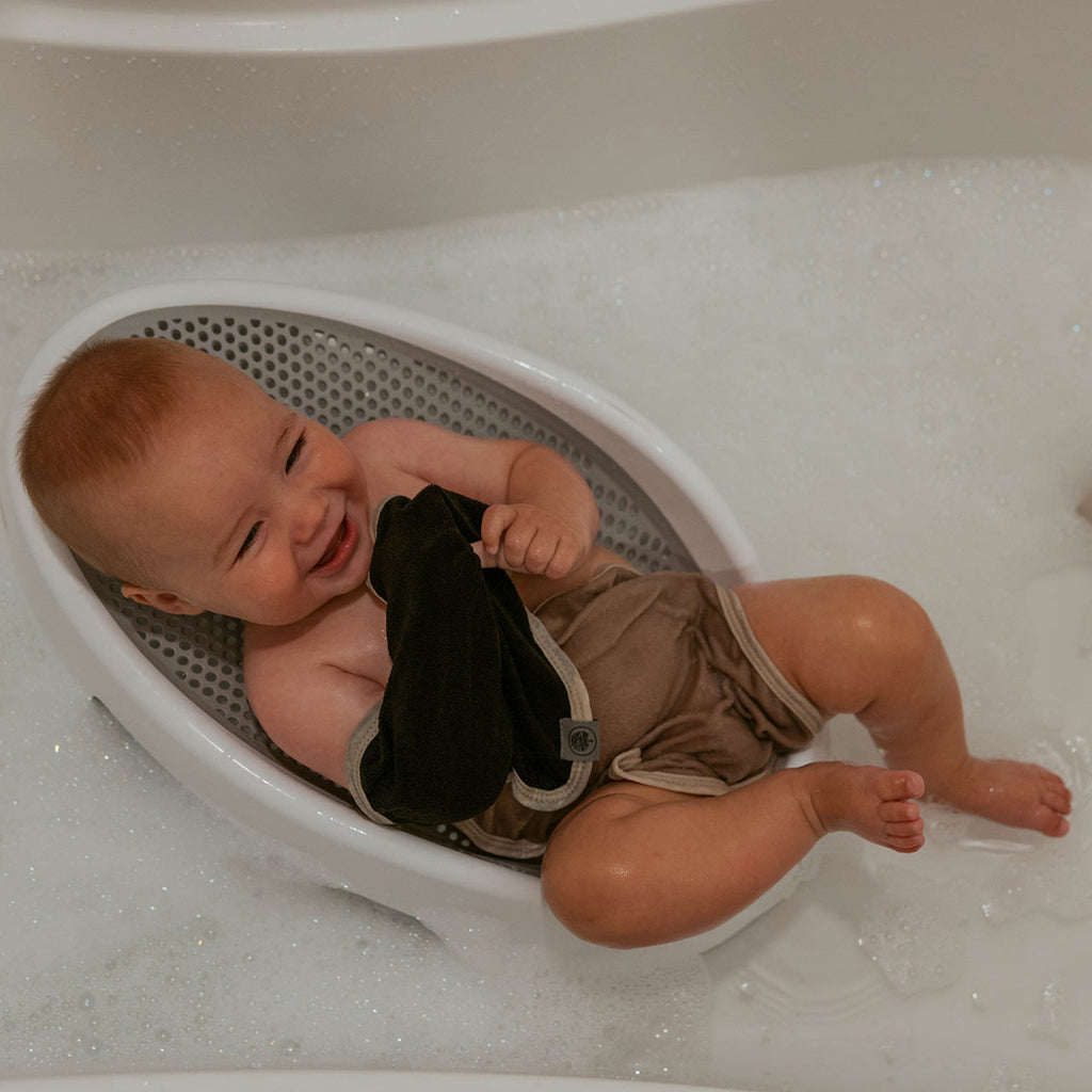 Baby in bathtub with dark terry washcloth in hand