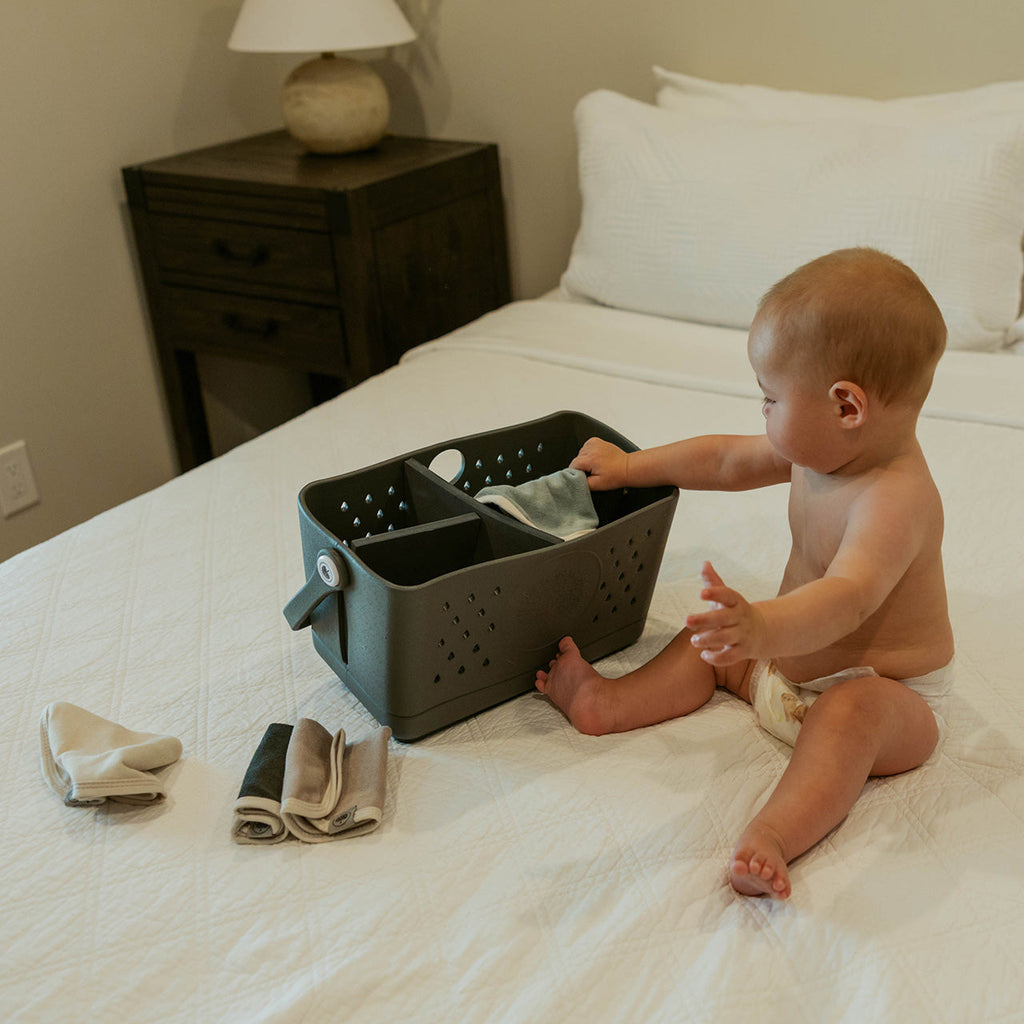 Baby playing near folded terry washcloths in a storage basket