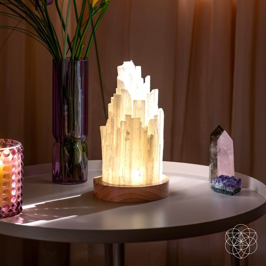 Selenite lamp on tabletop with glowing white crystal tower and round wooden base
