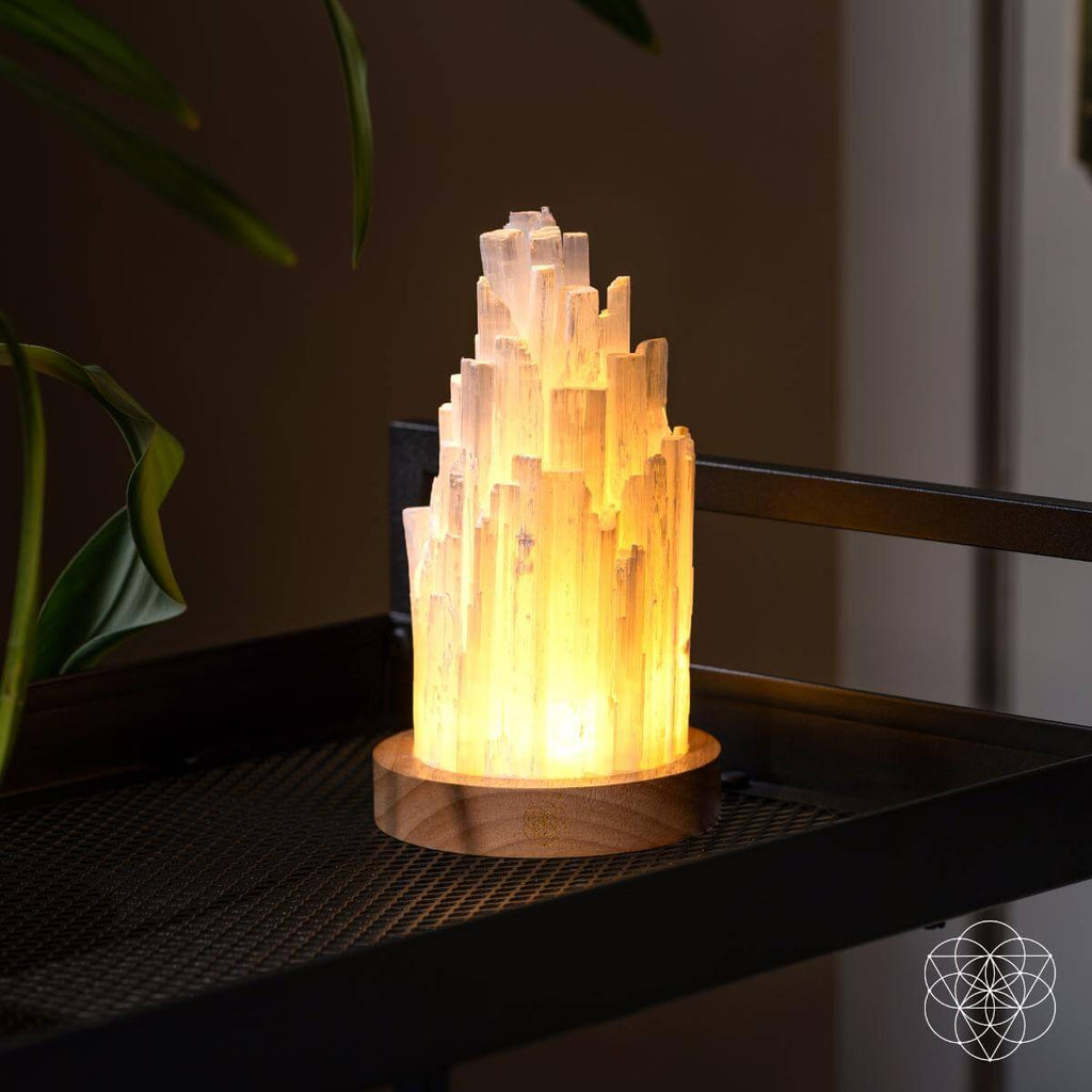 Selenite crystal lamp with warm glow and round wooden base on a dark shelf