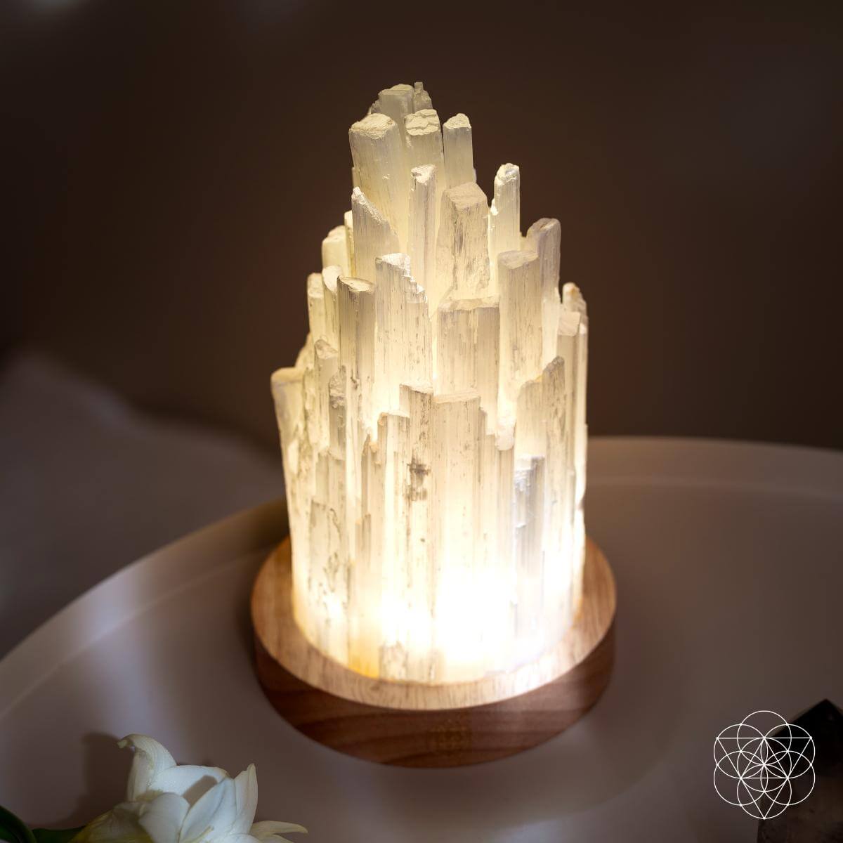 Close view of glowing selenite crystal lamp tower on round wooden base