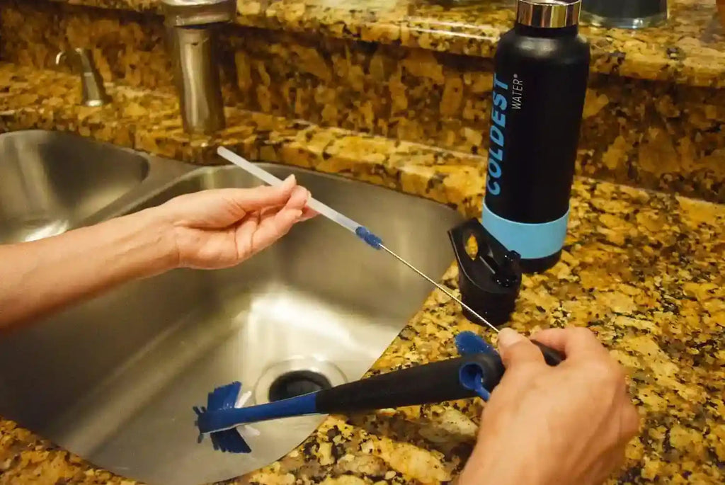 Blue bristle bottle brush with long handle held near a stainless sink