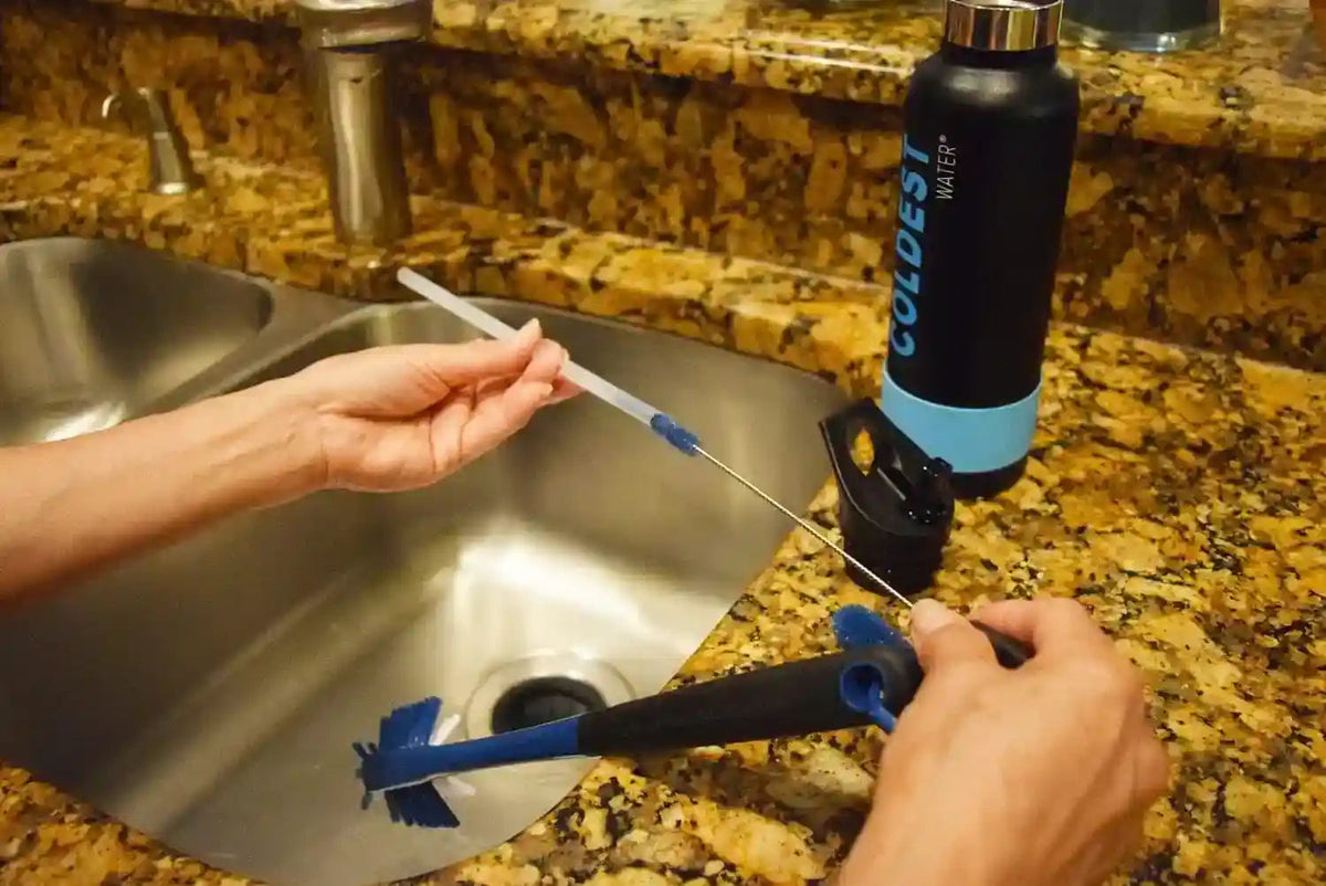 Blue bristle bottle brush with long handle held near a stainless sink