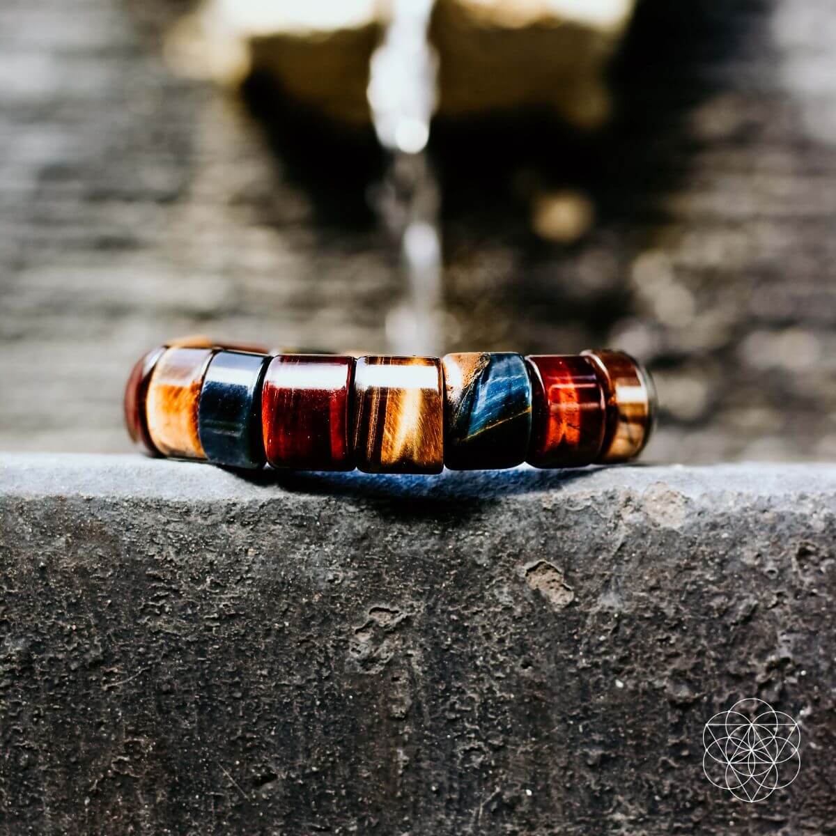 Multicolor bead bracelet lying on stone, with blue, red, and gold segments