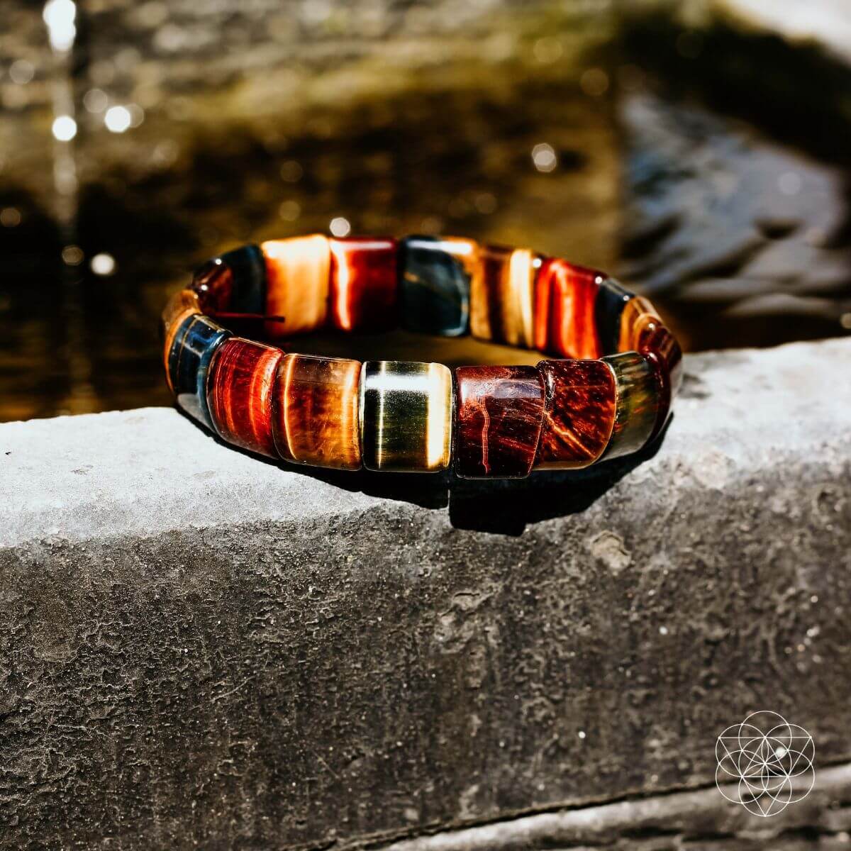 Multicolor bracelet with blue, red, and gold barrel beads on stone ledge