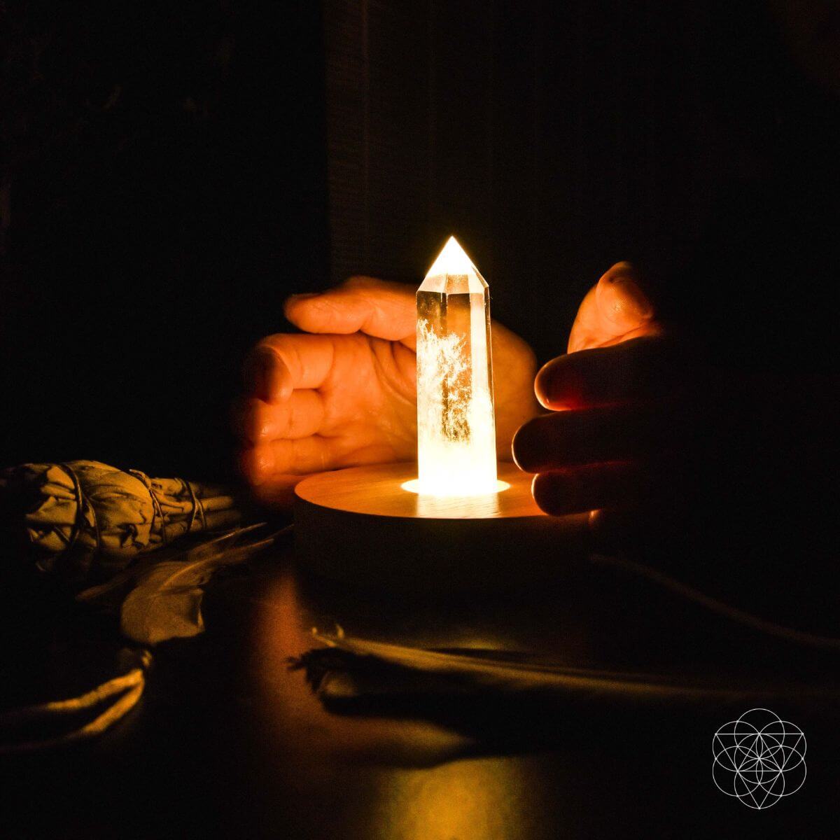 Healing lamp crystal point on round wooden base, shown being held by hands