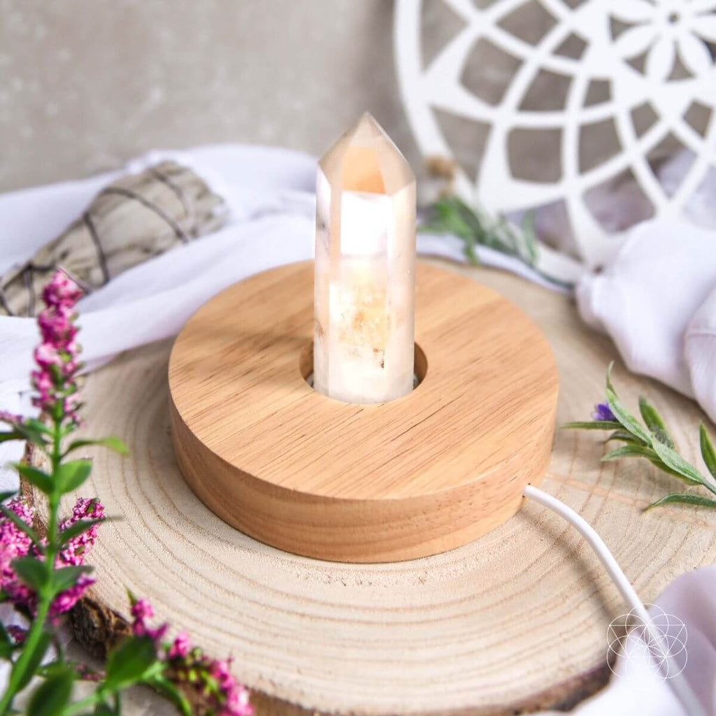 Healing lamp crystal point on round wooden base, lit on tabletop