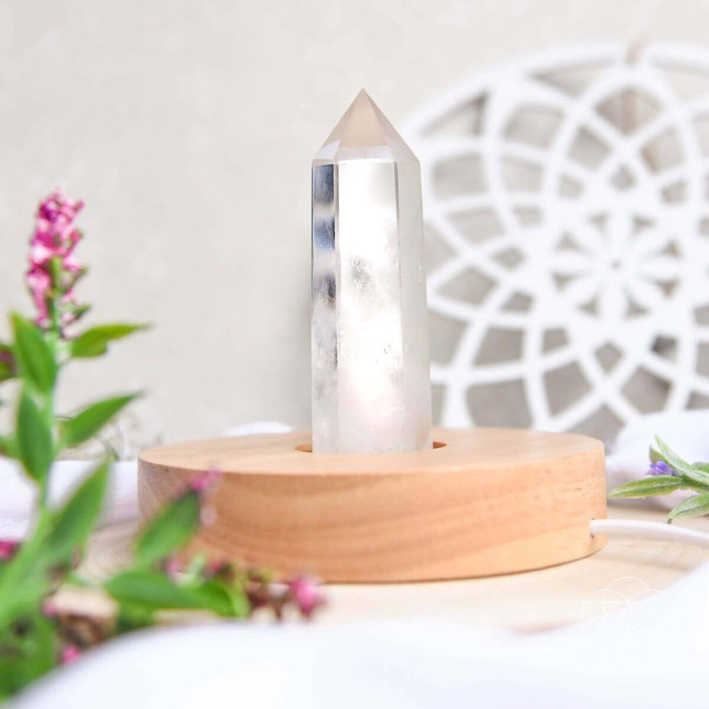 Healing lamp crystal point on circular wooden base, close-up on illuminated tip
