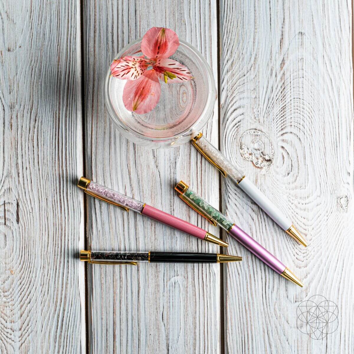 Crystal pen set with pink, green, and black pens and gold caps on a light wood table
