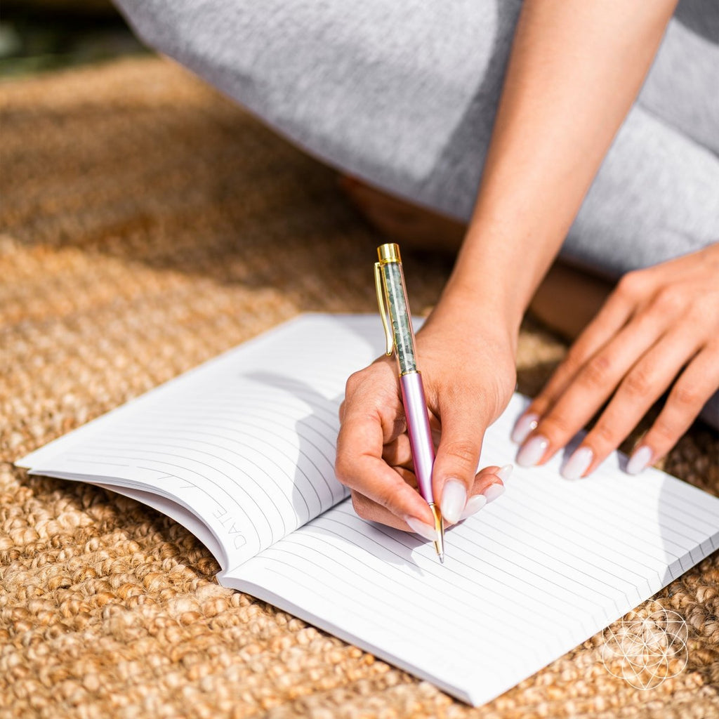 Self-cleansing crystal pen with pink barrel writing in a lined notebook on a couch