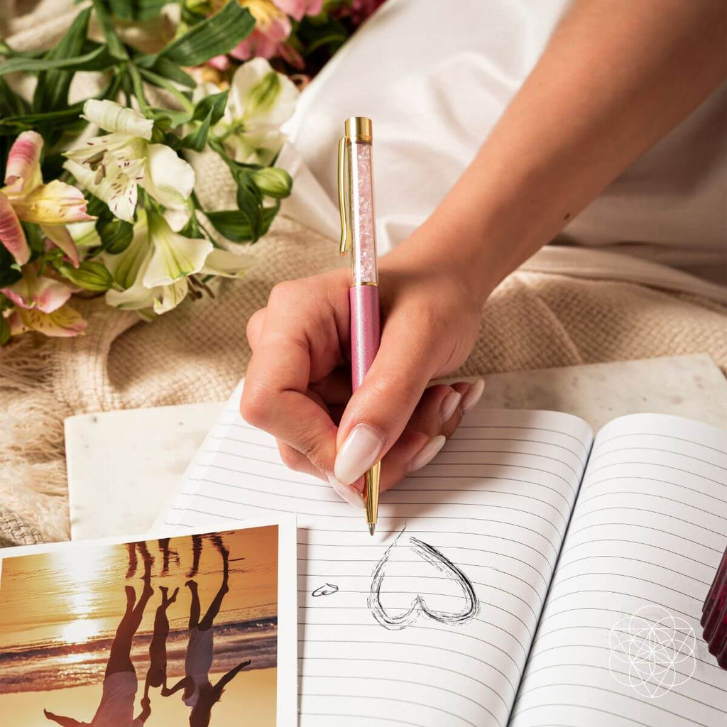 Self-cleansing crystal pen with pink barrel and gold cap held over lined notebook