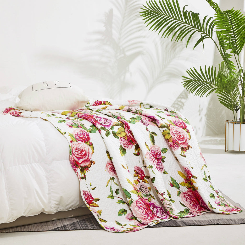 Quilted floral throw blanket with white base and pink rose pattern, folded drape