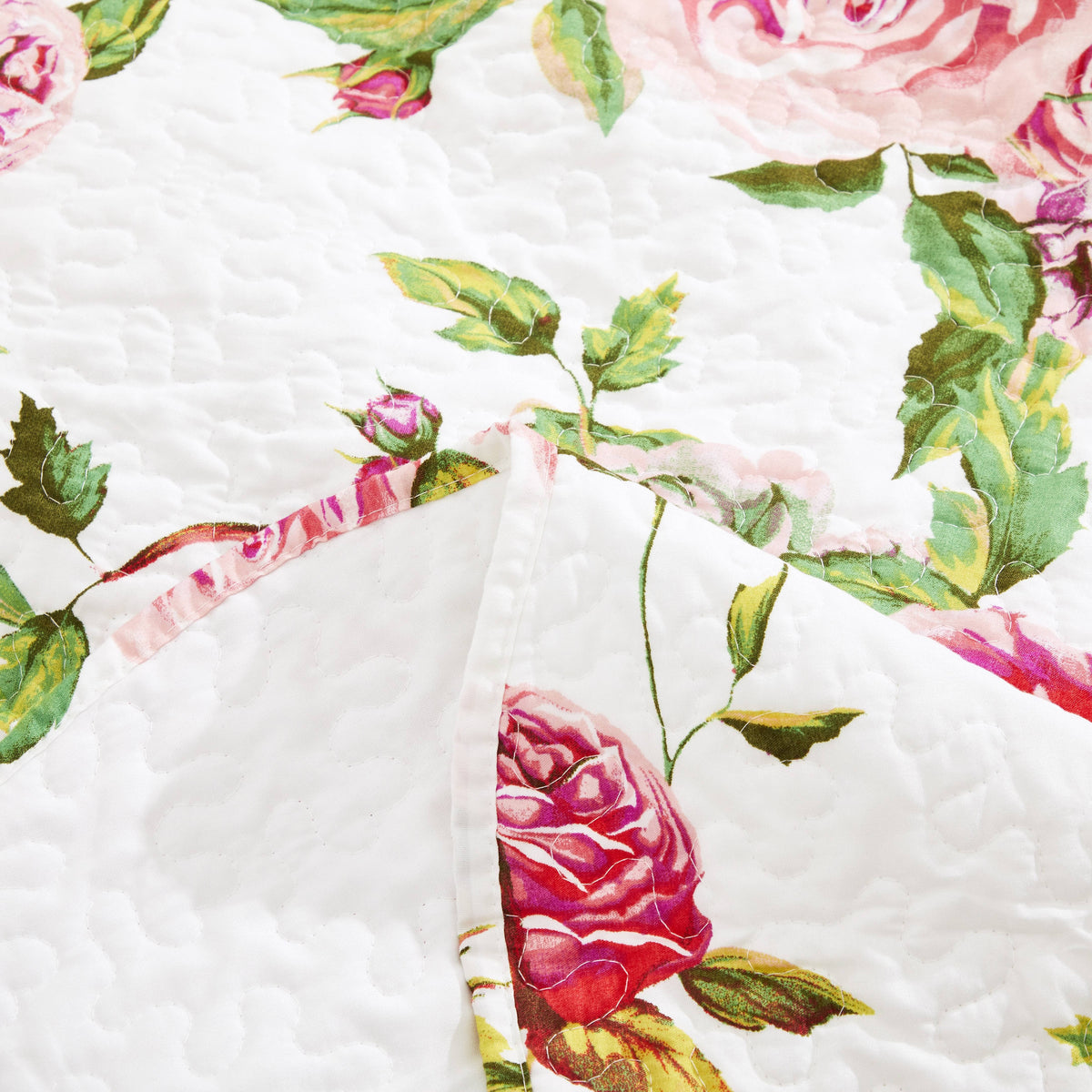 Close-up quilted fabric of white floral throw blanket with pink rose and green leaf print