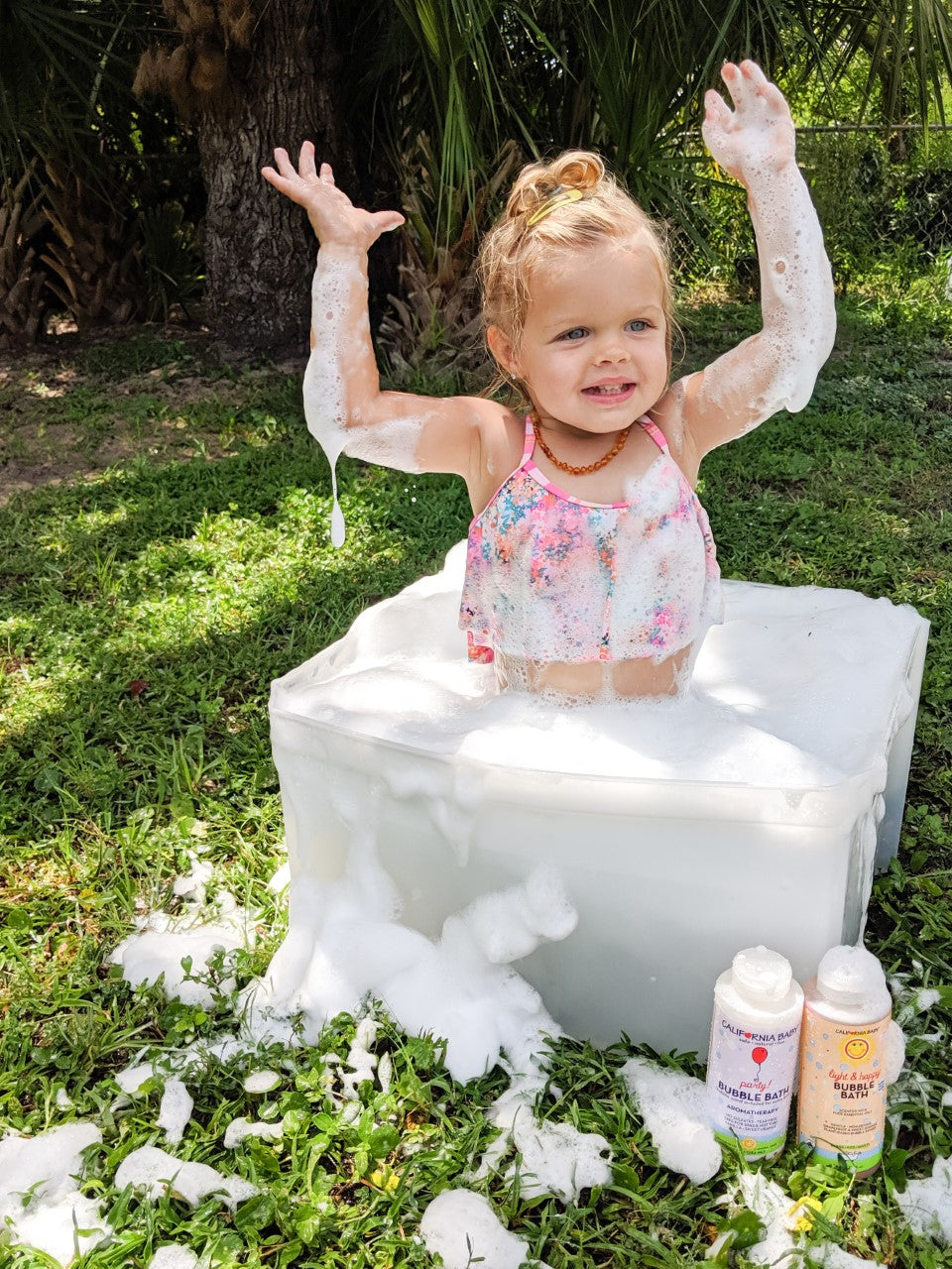 Bubble bath bottles on the ground with a child covered in foam and bubbles