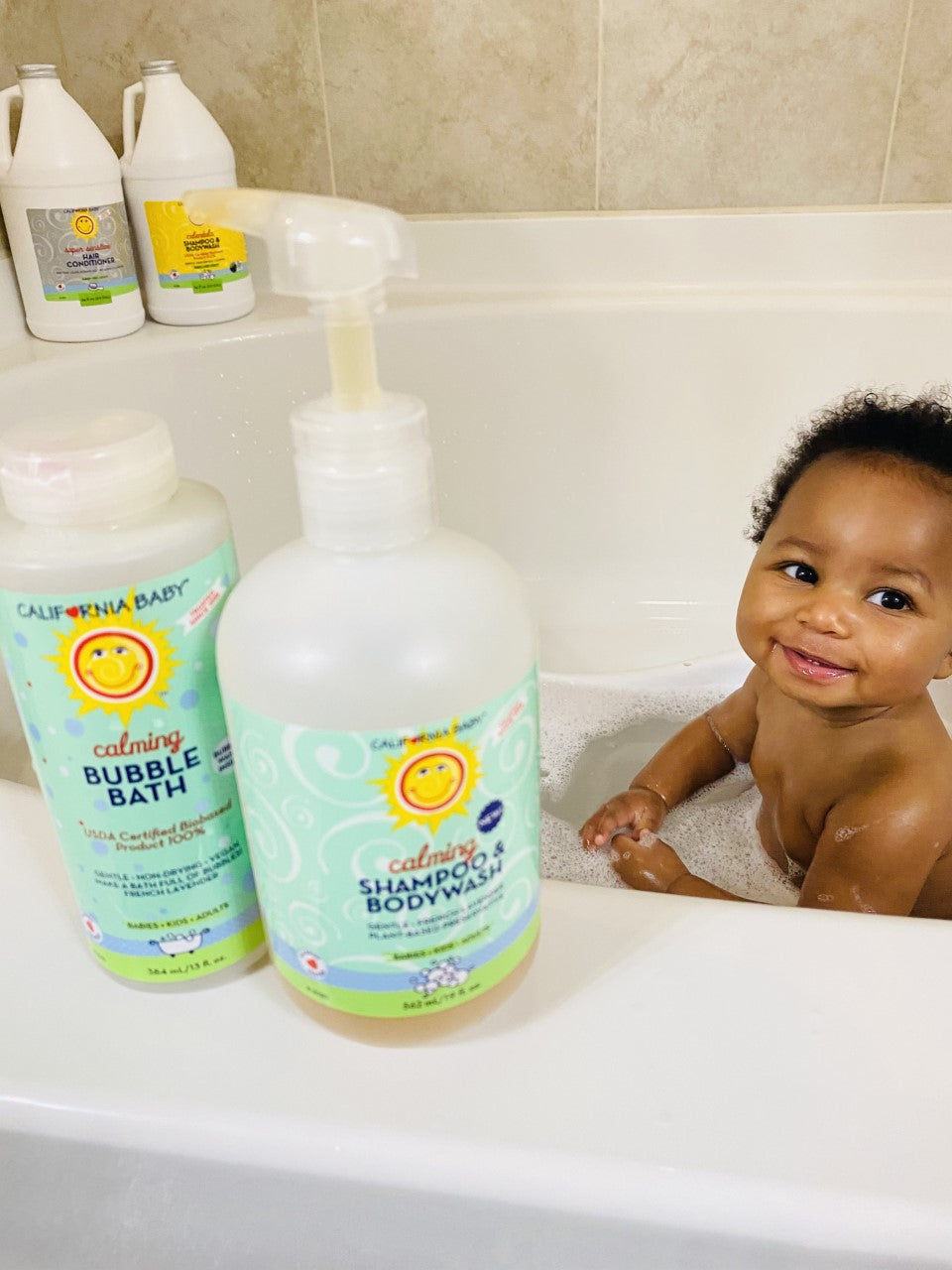 Bubble bath bottles on bathroom sink with foam and baby nearby