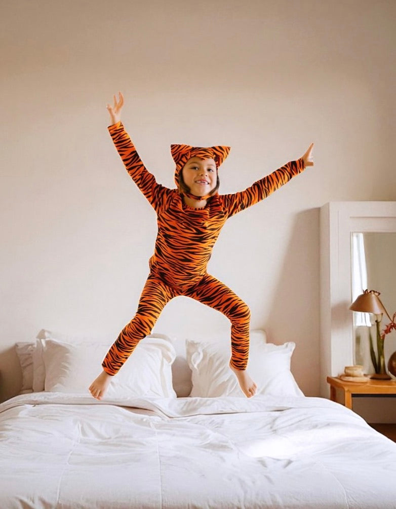 Kids tiger-print hooded jumpsuit costume with pointed ears and tail on bed