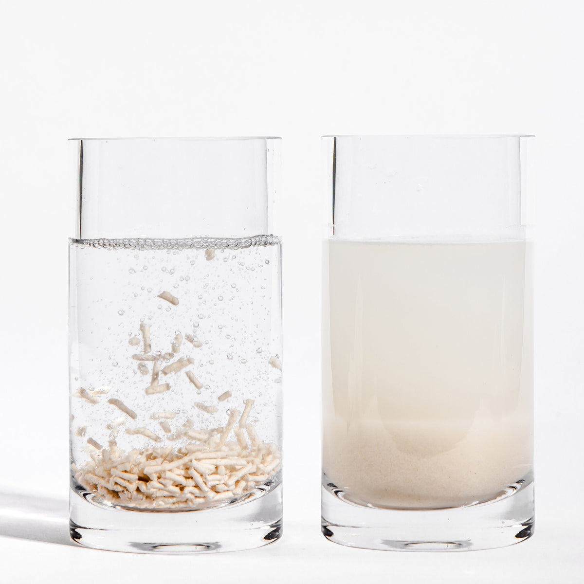 Clumping cat litter pellets shown in water, with a clear and cloudy glass
