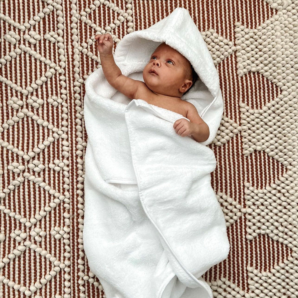 White hooded bath towel with baby wrapped in hooded robe, towel open across arms
