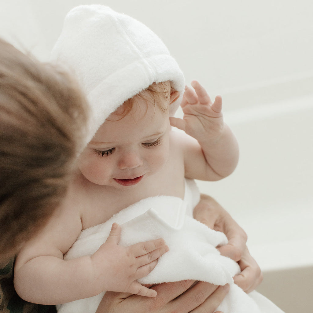 White hooded towel wrapped over a baby’s shoulders with small hood