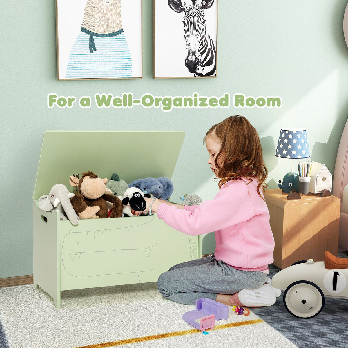 Green wooden kids toy box with safety hinge, lid open as toys are placed inside.