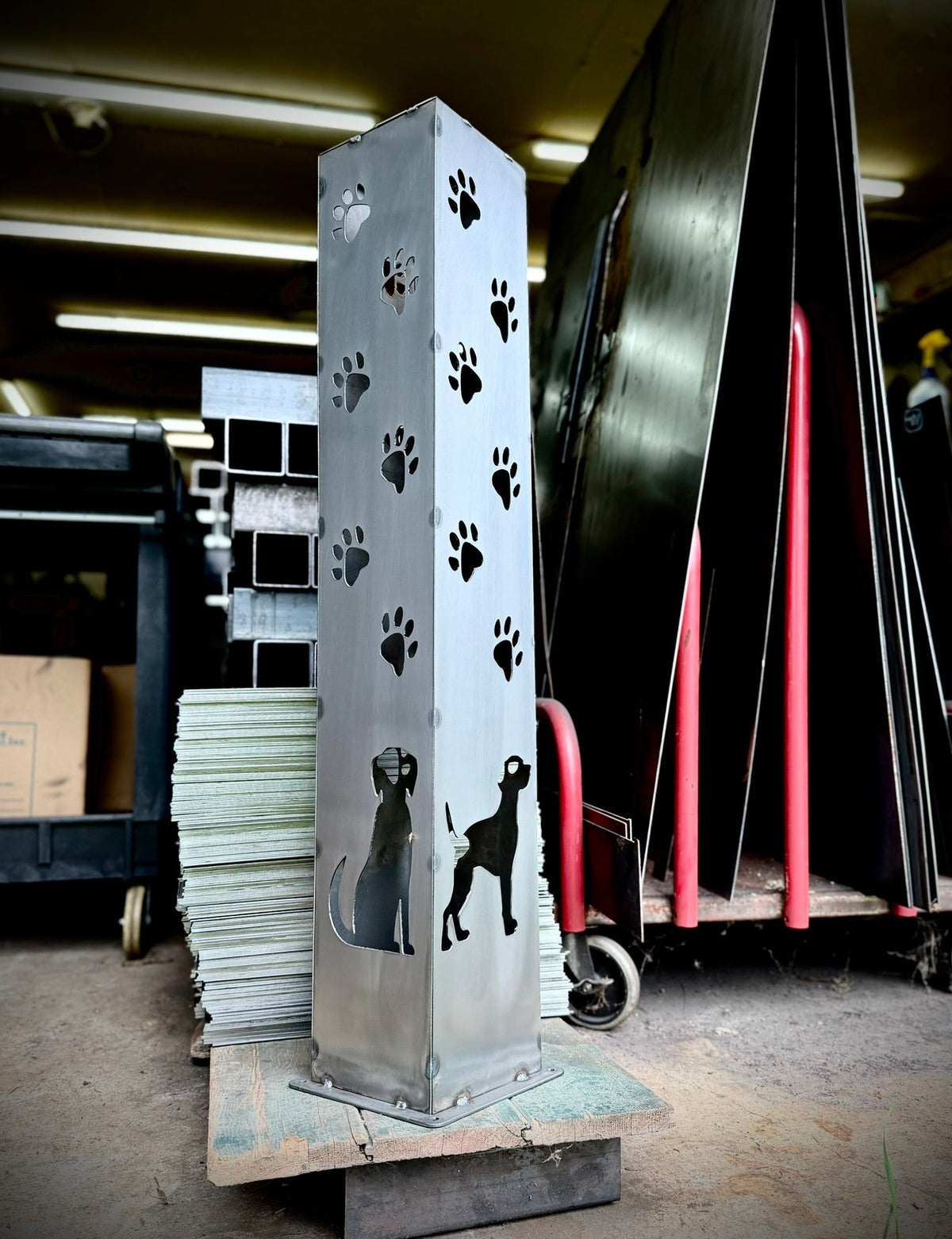 Steel solar pillar with paw-print decals and dog-and-cat silhouettes on a workshop pallet