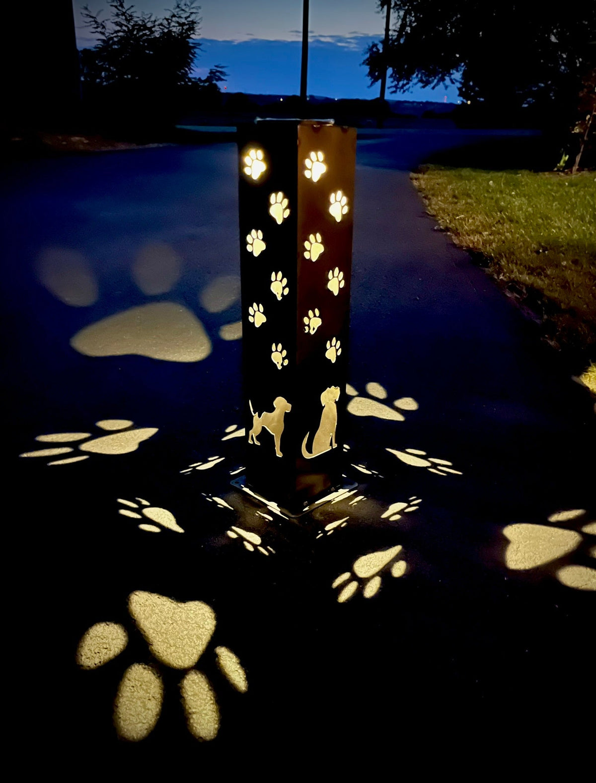Lit steel solar pillar showing paw-print and animal silhouettes cast in yard at night
