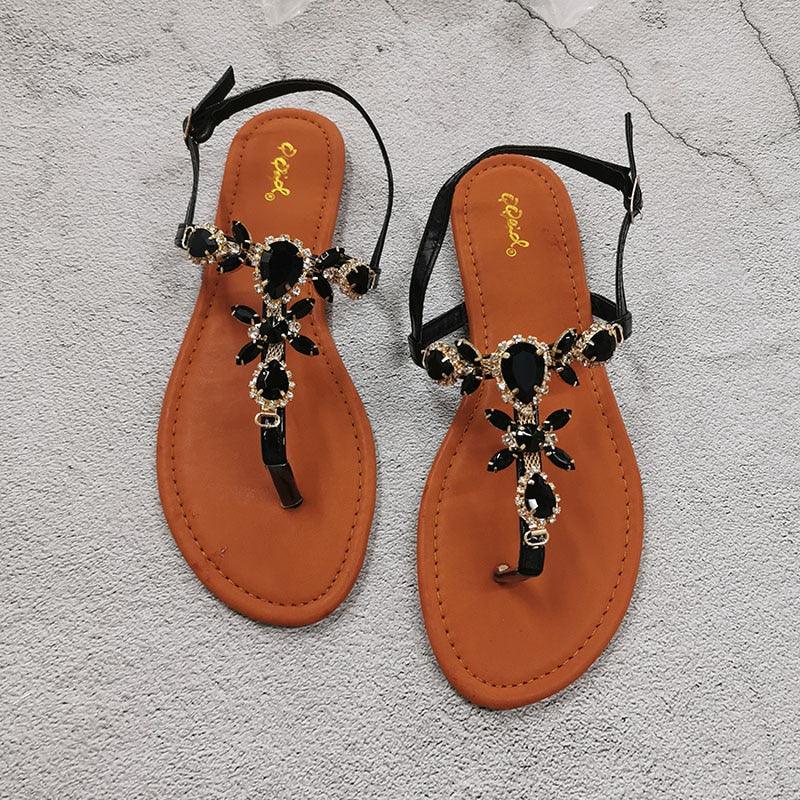 Black flat open-toe sandals with bow-like back straps and dark rhinestone flower details