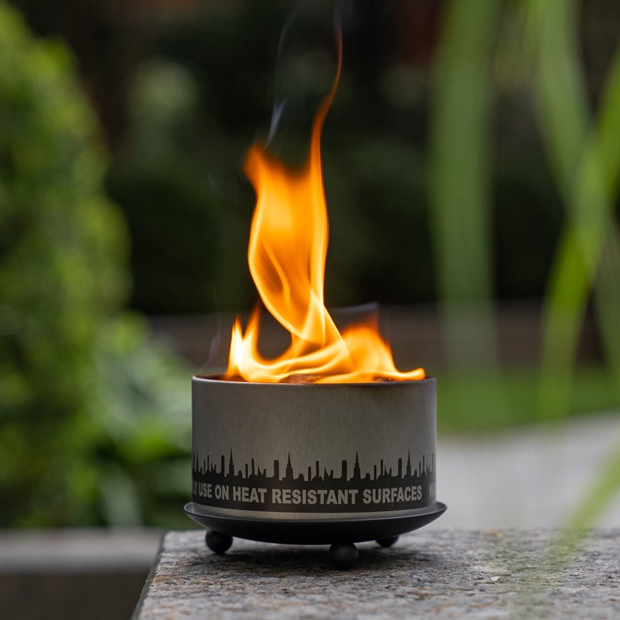 Round gray candle trivet with flame, skyline band detail, and three ball feet