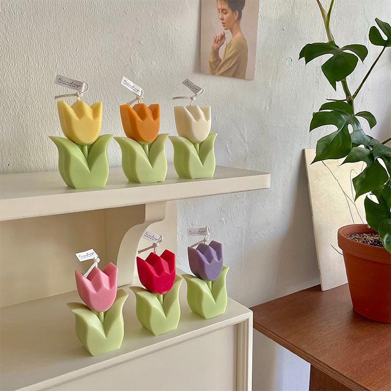 Handmade tulip flower-shaped candles arranged on shelves in pastel yellow, orange, and white